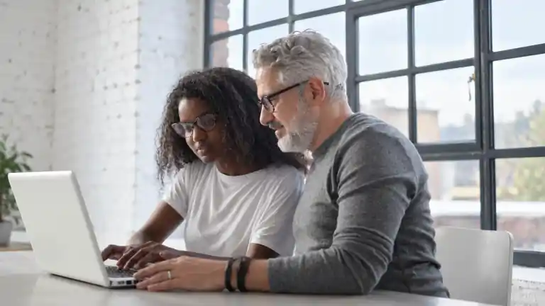 Two coworkers concentrating on a laptop at a shared table