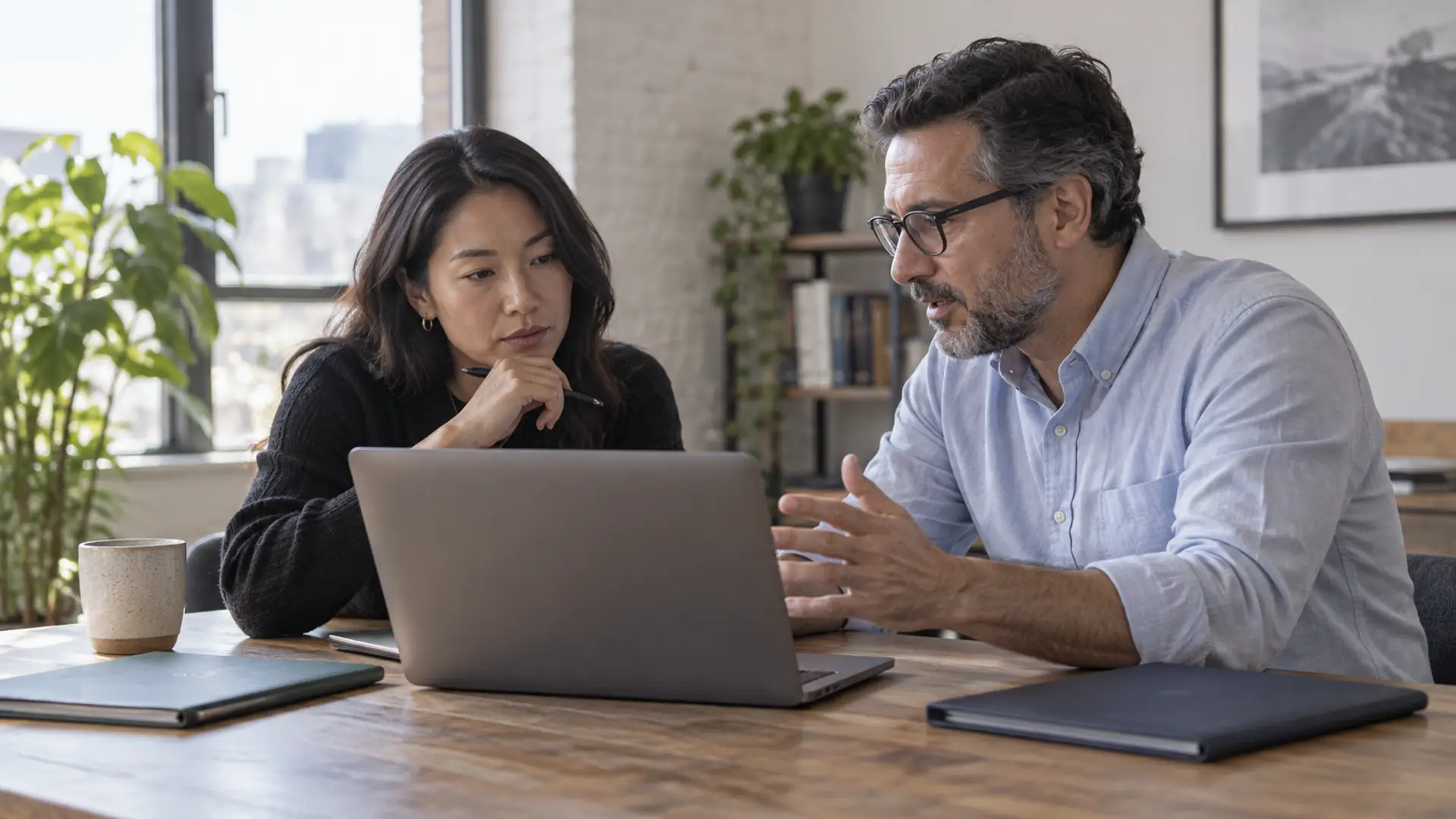 Two people comparing folders while using a laptop